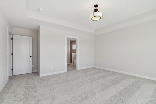 unfurnished bedroom featuring a tray ceiling, light colored carpet, ensuite bath, and baseboards