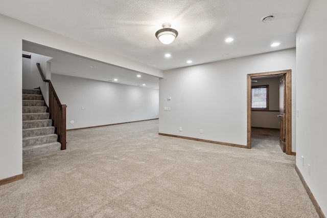 below grade area with baseboards, light colored carpet, stairs, recessed lighting, and a textured ceiling