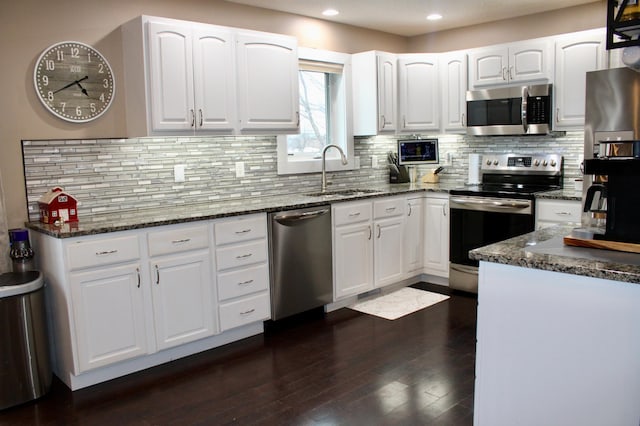 kitchen with dark wood-type flooring, a sink, white cabinetry, appliances with stainless steel finishes, and dark stone counters