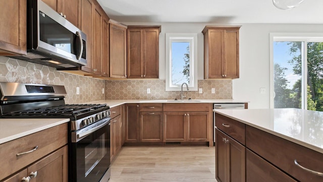 kitchen with a sink, light countertops, appliances with stainless steel finishes, light wood-type flooring, and backsplash