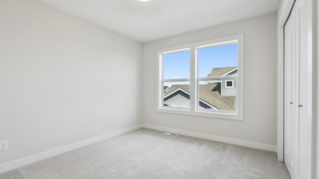 unfurnished bedroom featuring a closet, light colored carpet, visible vents, and baseboards