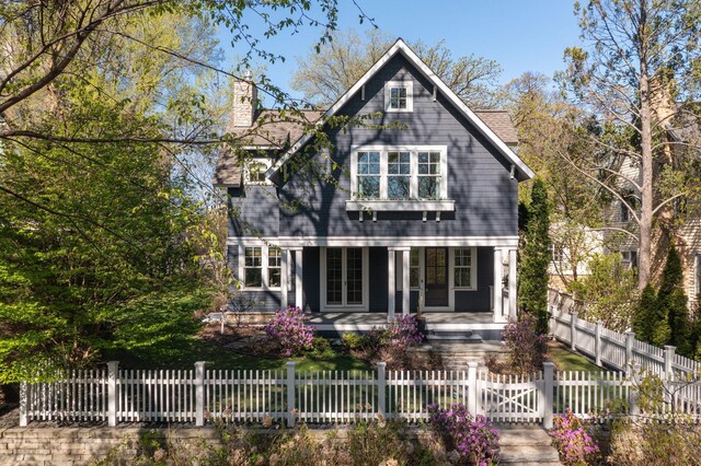 back of house featuring a porch, a chimney, and a fenced front yard