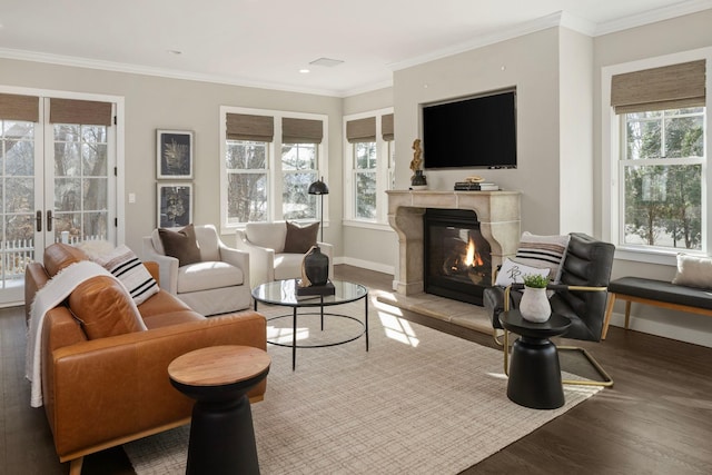 living room featuring plenty of natural light, wood finished floors, a tiled fireplace, baseboards, and ornamental molding