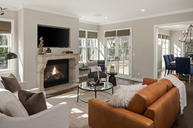 living area featuring wood finished floors, a high end fireplace, a chandelier, baseboards, and ornamental molding