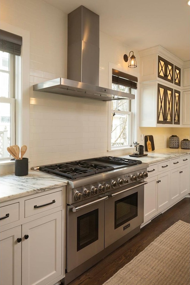 kitchen with wall chimney exhaust hood, double oven range, white cabinetry, and healthy amount of natural light