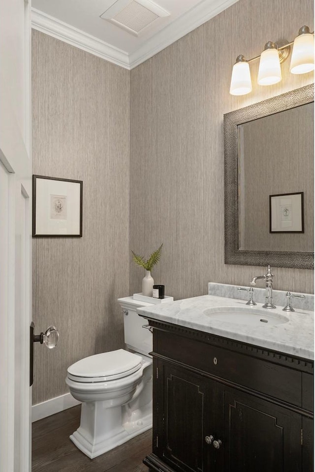 bathroom featuring toilet, crown molding, vanity, wallpapered walls, and wood finished floors