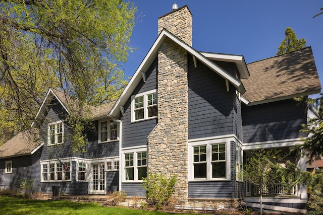 back of house featuring a chimney, a lawn, and roof with shingles