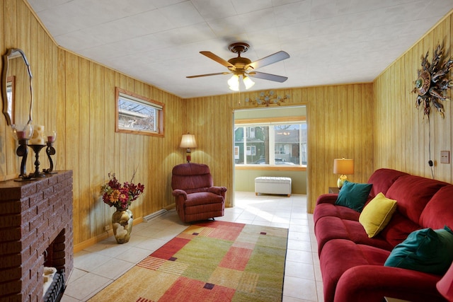 living area featuring a brick fireplace, light tile patterned floors, wooden walls, and ceiling fan