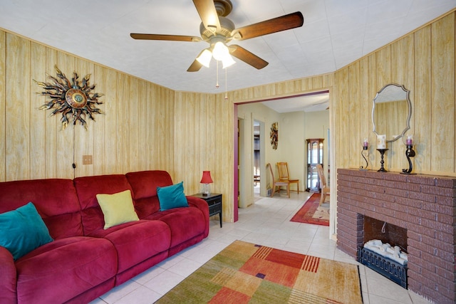 living room featuring a brick fireplace, wooden walls, light tile patterned flooring, and ceiling fan