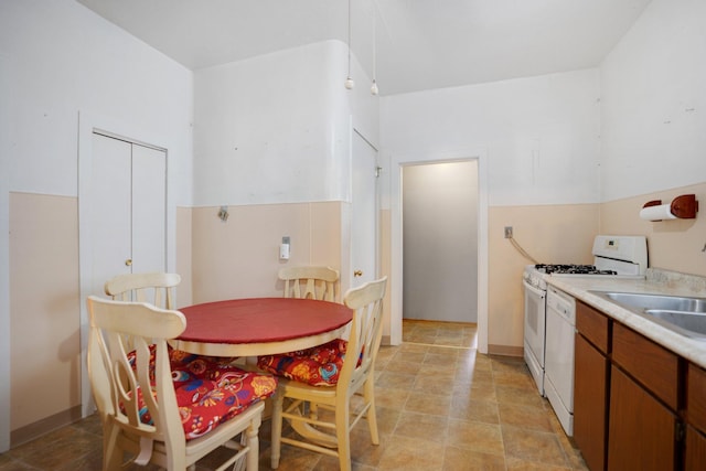 kitchen with white range with gas cooktop, brown cabinets, a sink, light countertops, and dishwasher