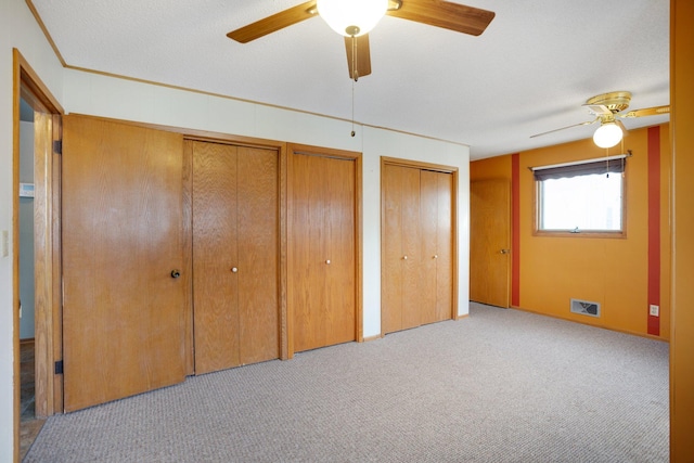 unfurnished bedroom with visible vents, carpet, multiple closets, and ceiling fan