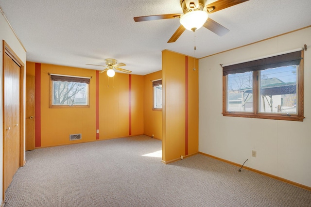 carpeted empty room featuring visible vents, baseboards, a textured ceiling, and a healthy amount of sunlight