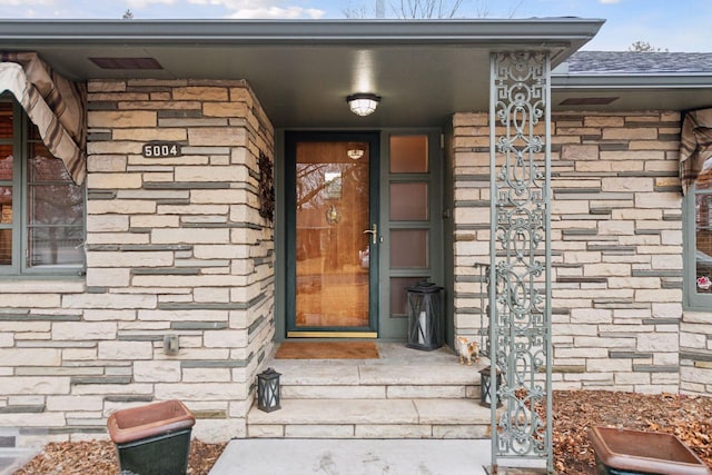 doorway to property with stone siding and a shingled roof