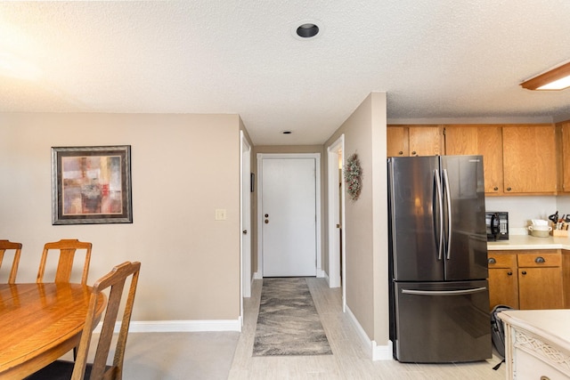 kitchen with brown cabinets, a textured ceiling, light countertops, and freestanding refrigerator