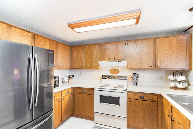 kitchen with under cabinet range hood, electric range, light countertops, and freestanding refrigerator