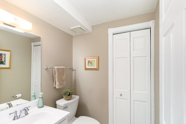 bathroom featuring vanity, toilet, a closet, and a textured ceiling