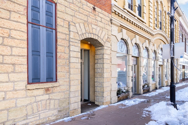 snow covered property entrance featuring brick siding and stone siding