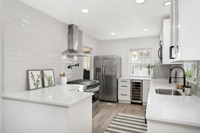 kitchen with wine cooler, a sink, light wood-style floors, appliances with stainless steel finishes, and wall chimney exhaust hood