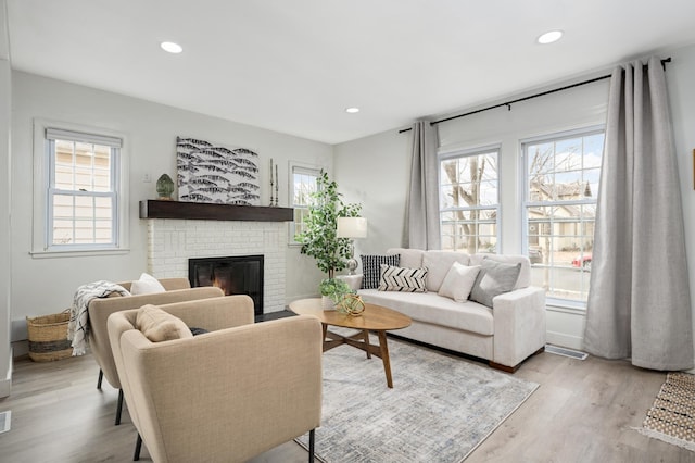 living room with recessed lighting, a brick fireplace, light wood-style flooring, and a healthy amount of sunlight