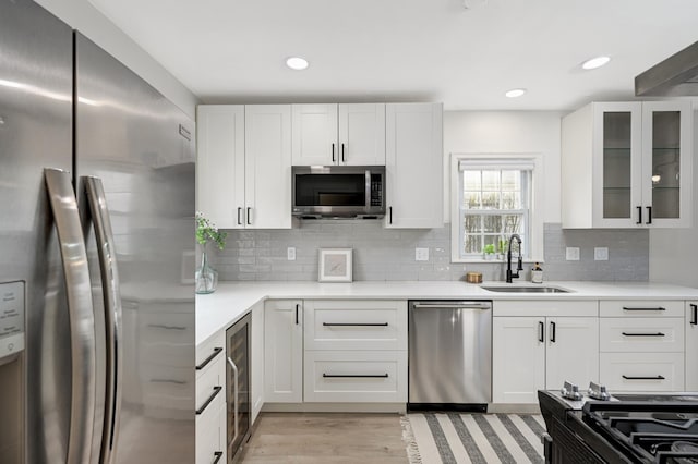 kitchen featuring stainless steel appliances, light countertops, glass insert cabinets, white cabinets, and a sink