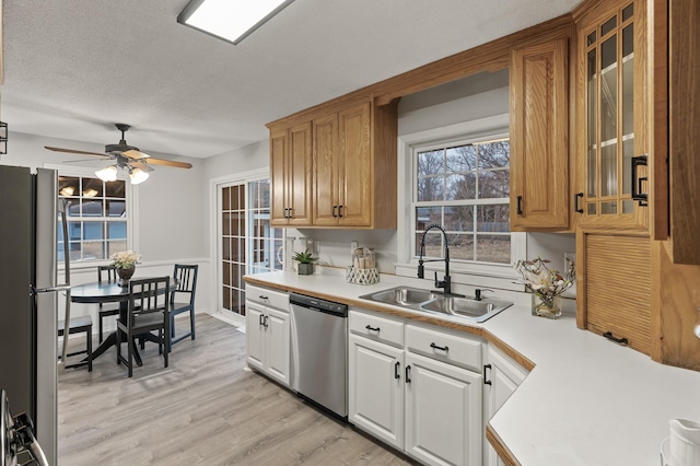 kitchen with glass insert cabinets, stainless steel appliances, light countertops, light wood-type flooring, and a sink