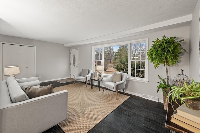 living area featuring a textured ceiling, dark wood-type flooring, visible vents, and baseboards