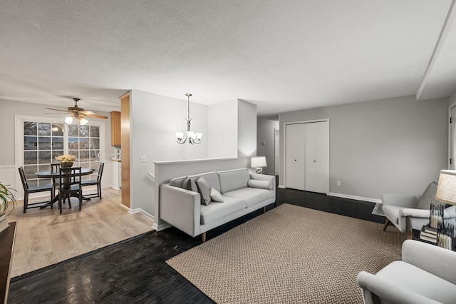 living area featuring dark wood-style floors, a textured ceiling, ceiling fan with notable chandelier, and baseboards