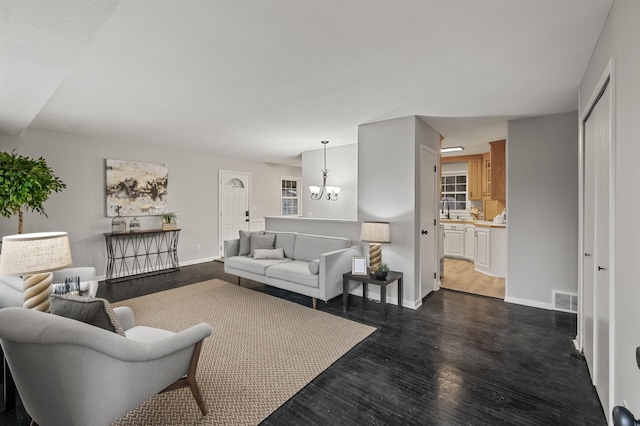 living area with visible vents, dark wood finished floors, baseboards, and an inviting chandelier