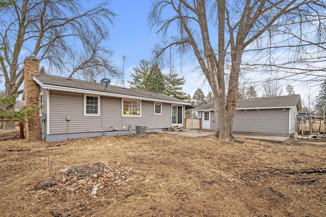 rear view of property with an outbuilding, a patio, central AC, fence, and a chimney