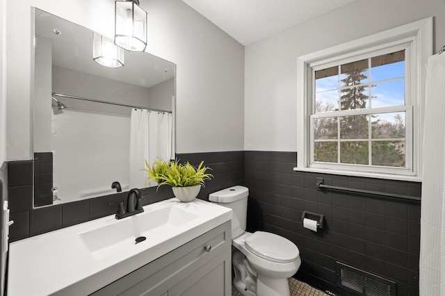 bathroom with visible vents, wainscoting, toilet, vanity, and tile walls