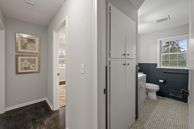 bathroom featuring a textured ceiling, toilet, vanity, visible vents, and tile walls