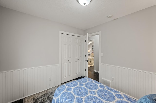 bedroom with a closet, wainscoting, visible vents, and a textured ceiling