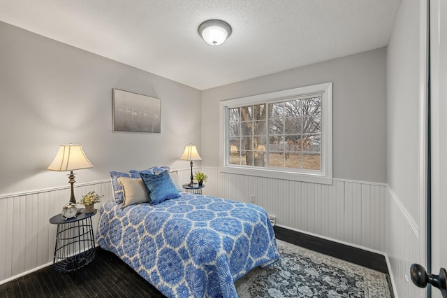 bedroom with a textured ceiling, wood finished floors, and wainscoting