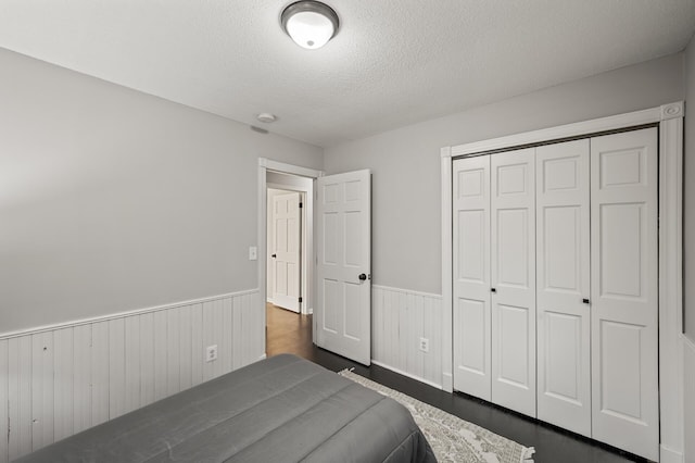 unfurnished bedroom featuring a wainscoted wall, dark wood-style flooring, a textured ceiling, and a closet