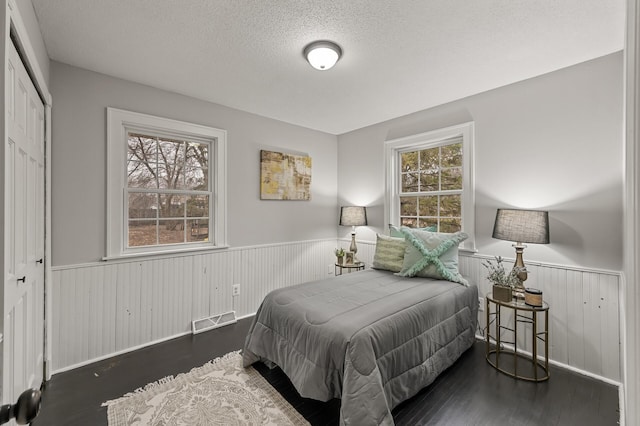 bedroom with wainscoting, visible vents, multiple windows, and wood finished floors