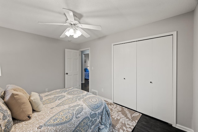 bedroom featuring dark wood-style flooring, visible vents, baseboards, a ceiling fan, and a closet