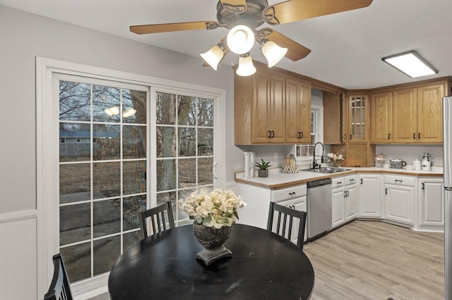 kitchen with light countertops, light wood-style floors, glass insert cabinets, a sink, and dishwasher