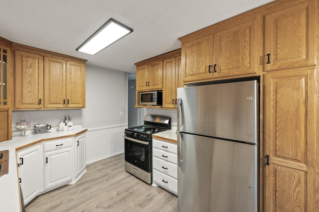 kitchen featuring light wood-type flooring, appliances with stainless steel finishes, light countertops, and glass insert cabinets