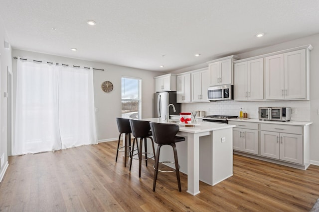 kitchen featuring a kitchen breakfast bar, light wood-style flooring, a center island with sink, and stainless steel appliances