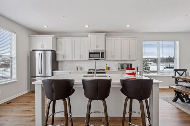 kitchen with tasteful backsplash, light wood-type flooring, light countertops, stainless steel appliances, and a kitchen island with sink