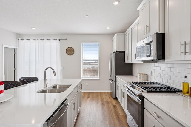 kitchen with backsplash, stainless steel appliances, light countertops, and a sink