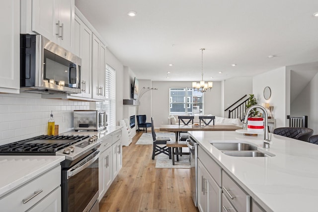 kitchen featuring light wood-type flooring, a sink, open floor plan, stainless steel appliances, and decorative backsplash