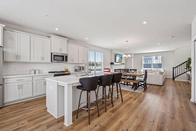 kitchen featuring light wood-type flooring, a breakfast bar, a sink, tasteful backsplash, and appliances with stainless steel finishes