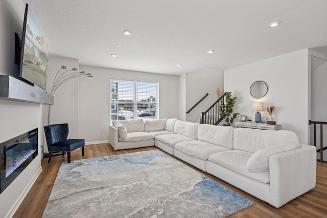 living room featuring stairway, wood finished floors, baseboards, recessed lighting, and a glass covered fireplace