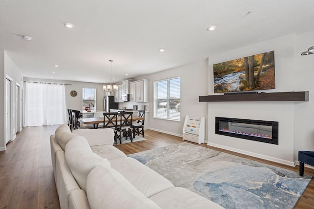 living room with a notable chandelier, a glass covered fireplace, wood finished floors, recessed lighting, and baseboards