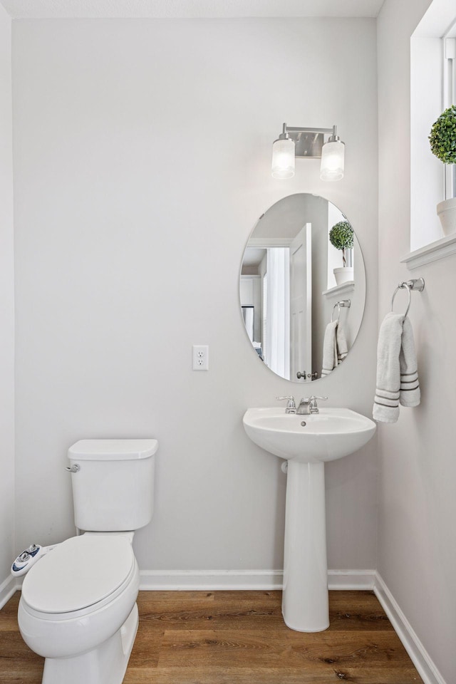 half bath featuring toilet, baseboards, and wood finished floors