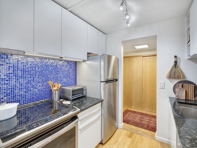 kitchen with light wood-style flooring, stainless steel appliances, white cabinetry, decorative backsplash, and dark stone countertops