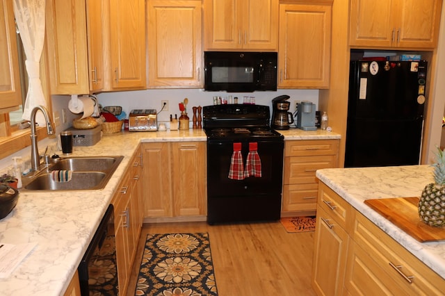 kitchen with black appliances, light wood finished floors, and a sink