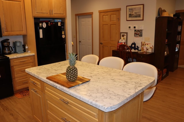 kitchen with light wood finished floors, a kitchen island, a breakfast bar, black appliances, and light countertops