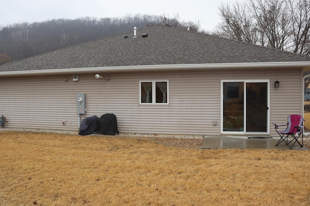 back of house featuring a lawn and roof with shingles